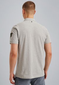 Polo de color gris claro con mangas cortas, un cuello y un parche en el hombro izquierdo. Material de algodón suave con un dobladillo recto.