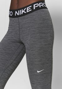 Grå atletiska tights med en melerad textur, med en svart midja som har "NIKE PRO" i vit text och en liten vit Nike-logotyp.