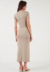 Completo beige a due pezzi che presenta un top aderente con maniche corte e una gonna lunga e aderente in un tessuto morbido e liscio. Dettagli di design minimi.