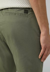 Olivgrüne Baumwollhose mit geradem Schnitt, Gesäßtasche und kleinem geprägtem Logodetail am Bund. Glatte Textur, mittlere Leibhöhe.