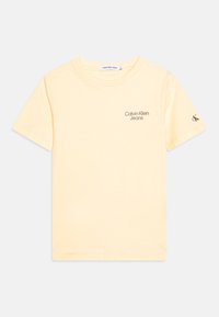 Světle žluté bavlněné tričko s krátkým rukávem, na hrudi je šedé logo "Calvin Klein Jeans" a malé logo na rukávu.