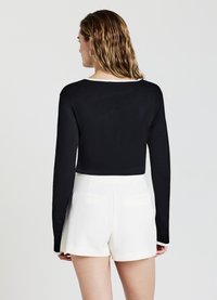 Schwarzes langärmeliges Crop-Top mit weißem Kragen, kombiniert mit weißen High-Waist-Shorts mit zwei Gesäßtaschen. Glatte Textur.