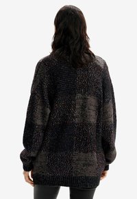 Överdimensionerad stickad tröja i mörka nyanser med strukturerad lapplösning. Har långa ärmar, ribbade ärmslut och en avspänd passform.