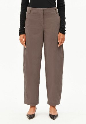 Woman wearing loose-fitting brown corduroy pants with front pockets paired with black long-sleeve top and black pointed shoes.