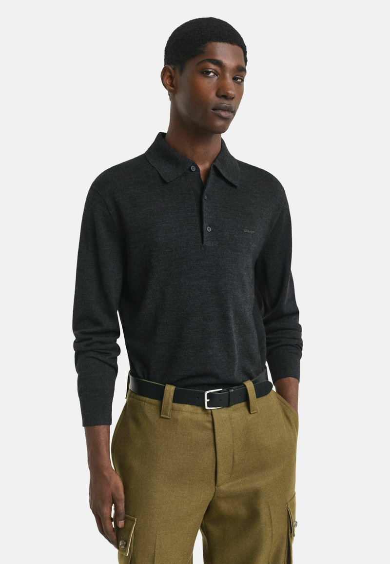 Zwarte langslavige polo met een kraag en twee knopen, gemaakt van zachte stof, gecombineerd met olijfgroene broek met zijzakken.