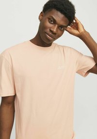 Lichtroze T-shirt met korte mouwen van zacht materiaal. Heeft een klein wit logo op de linkerkant van de borst en een klassieke ronde hals.