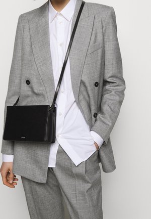 Grå dubbelknäppt kostymjacka med matchande byxor, bärs över en vit skjorta. En liten svart axelväska syns också.