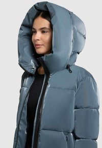 Padded jacket w kolorze szarym z dużym, strukturalnym kapturem. Posiada zamek błyskawiczny z przodu oraz teksturowany materiał z pikowanymi sekcjami.