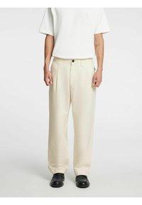 Lyse kremhvite, løstsittende bukser med rett snitt, utstyrt med en enkelt knappelukking og to sidelommer. Brukt sammen med svarte sko.