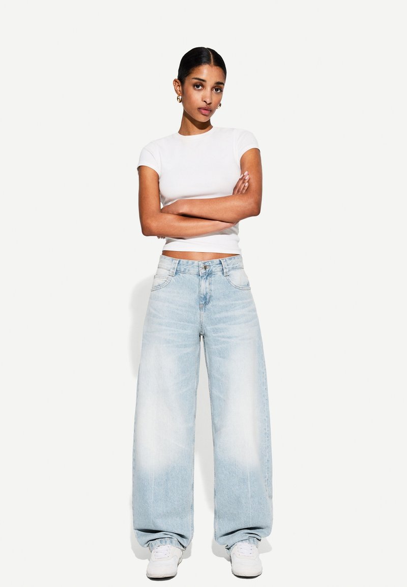 Lyseblå vide jeans med en falmet finish, parret med en tætsiddende hvid t-shirt. Outfittet kompletteres af hvide sneakers.