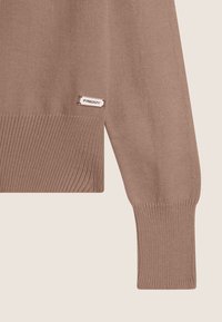 Pull en tricot marron avec des poignets et un ourlet côtelés, arborant une petite étiquette logo "Freddy" cousue sur le côté inférieur.
