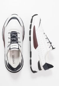 Sneakers bianchi con accenti neri e bordeaux. Realizzati in pelle e mesh, presentano un design testurizzato, perforazioni traspiranti e lacci.