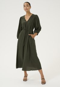 Vestido largo de color verde oliva, hecho de material ligero, con escote en V, cierre de botones en la parte delantera, mangas abullonadas, cintura ceñida con cinturón y bolsillos laterales.