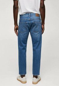 Jeans de mezclilla azul con corte recto, que cuentan con bolsillos traseros y una etiqueta de cuero marrón en la cintura trasera.