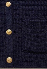 Tissu en maille bleu marine foncé avec trois boutons dorés ornés et une poche carrée tricotée assortie.