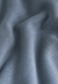 Puha, textúrált anyag egy tompa kék árnyalatban, sima felülettel, finom bordás mintázattal.