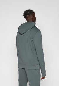 Sweatshirt cinza com capuz, feito de material suave e com um corte descontraído. Apresenta um bolso tipo canguru e punhos canelados, mostrado pela parte de trás.