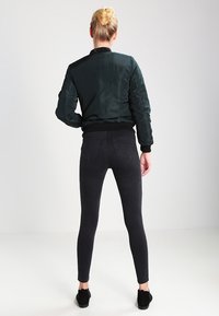 Svart bomberjacka med en slät yta, tillsammans med mörka smala jeans. Outfiten har en ribbad midja och en mjuk textur.