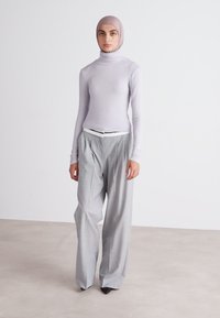 Helllila gerippter Rollkragenpullover, kombiniert mit lockeren, grauen Hosen. Ein weißer Gürtel betont die Taille. Glattes Gewebe und maßgeschneiderter Look.
