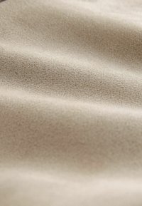 Tissu beige avec une surface douce et texturée, présentant de légères rides et un motif granuleux fin. Convient pour le revêtement de meubles ou les vêtements.