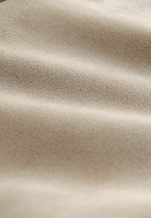 Tissu beige avec une surface douce et texturée, présentant de légères rides et un motif granuleux fin. Convient pour le revêtement de meubles ou les vêtements.