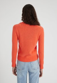 Pull en tricot orange avec un col rond, des poignets et un ourlet côtelés. La vue arrière montre une texture lisse et une silhouette légèrement ajustée.