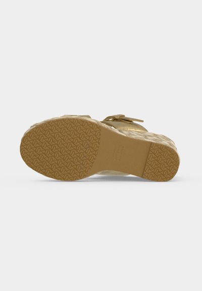 Semelle d'une sandale compensée beige avec semelle en caoutchouc et boucle décorative sur la partie supérieure, vue de dessous sur fond uni.