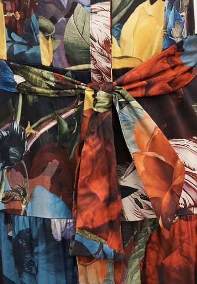 Lillemustriga kangas sisaldab erksaid värve nagu punane, roheline, sinine ja kollane. Disaini lõpetab vöökohal sõlmitud detail.