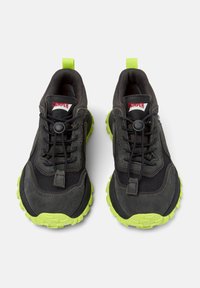 Czarno-szare buty sportowe z teksturowanym wykończeniem i fluorescencyjnozielonymi gumowymi podeszwami. Posiadają system sznurowania oraz żółtą pętelkę do zakupu.