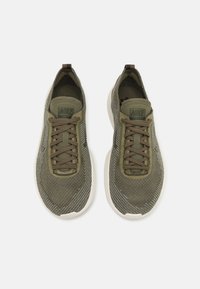 Sneaker Nike con un upper in maglia verde oliva, presentano un design testurizzato, allacciatura frontale e una suola in gomma bianca.