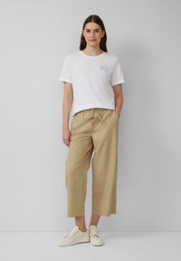 Witte katoenen t-shirt met kleine tekst "ZOMER", gecombineerd met beige cropped broeken en witte veterschoenen.