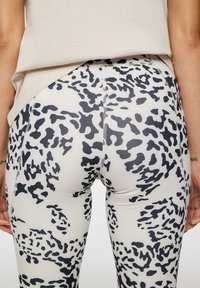 Leggings a vita alta in tessuto crema con una stampa leopardata astratta nera, accompagnati da cuciture piatte per un comfort aggiuntivo.