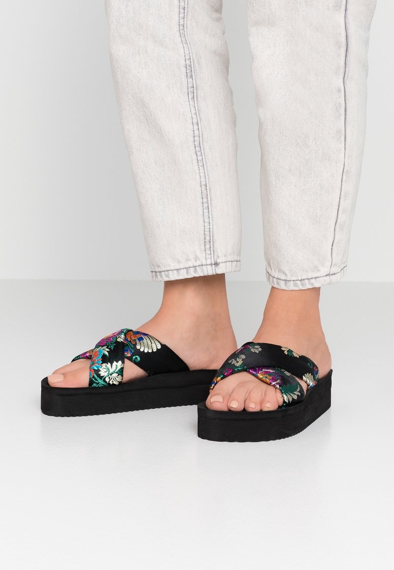 Černé platformové sandály s vyšívaným květinovým vzorem v živých barvách, s překříženým páskem a texturovanou podrážkou.