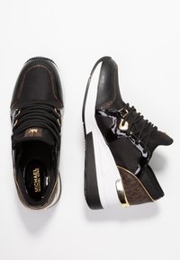 Czarne sneakersy z teksturowanej tkaniny i akcentami z lakierowanej skóry, z białą podeszwą i złotymi detalami.