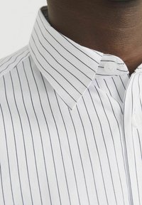 White cotton shirt with narrow navy vertical stripes. Features a classic collar and button closure, with a smooth, textured fabric.