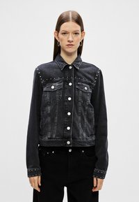 Musta farkkutakki, jossa on hopeiset napit, niittikoristeet harteilla ja hihansuissa, klassinen kaulus ja kaksi rintataskua.