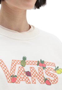 Sudadera de algodón blanca con un gran logo de "VANS" en color naranja y diseño a cuadros, adornado con coloridas ilustraciones de frutas, incluyendo fresas y piñas.