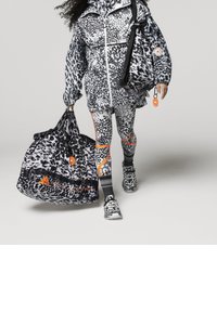 Leopardmönstrad jacka, leggings och väska i svart och vitt med orange detaljer. Texturerat material och sportig design, bärs med matchande skor.