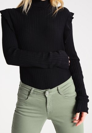 Pull noir à col roulé à côtes avec des accents de manches à volants, associé à un jean vert clair avec poches avant et fermeture à boutons.