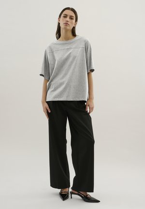 Hellgraues, oversized T-Shirt mit kurzen Ärmeln und horizontaler Nahtdetail, kombiniert mit schwarzen, weit geschnittenen Hosen und schwarzen Slingback-Absätzen.