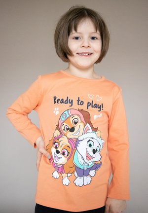 Maglietta a maniche lunghe arancione con cani dei cartoni, con la scritta "Pronti a Giocare!" in blu. Il design include tre cani con caratteristiche animate.