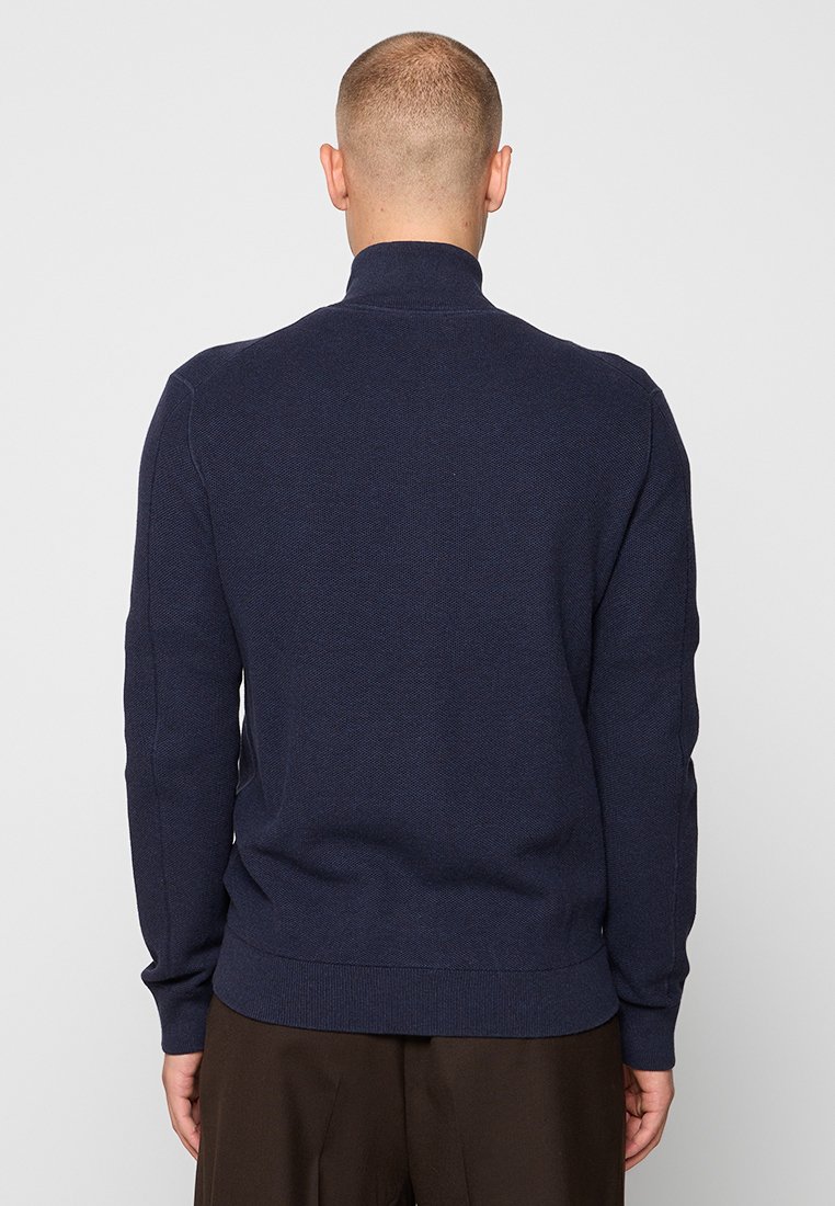 Navi-blauer Strickpullover mit hohem Kragen, gerippten Bündchen und Saum. Strukturierte Stoff mit figurbetontem Design und sauberen Nähten.