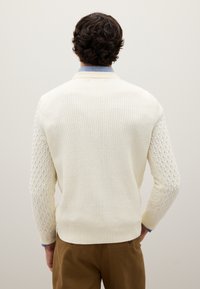 Leicht cremiger Strickpullover mit Rippenstruktur am Körper und einem Rautenmuster an den Ärmeln. Abgerundet mit einem Rundhalsausschnitt und einem festen Saum.