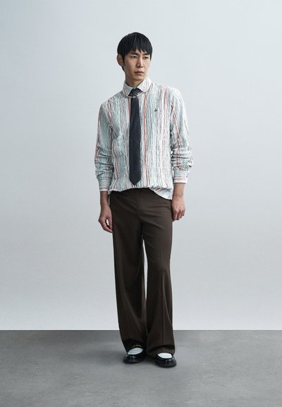 Ριγέ, υφασμένο λευκό και πράσινο πουκάμισο με πορτοκαλί γραμμές, συνδυασμένο με καφέ παντελόνια φαρδιάς γραμμής και μαύρα παπούτσια με λευκές λεπτομέρειες.