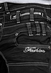 Jeans in denim nero con cuciture bianche, caratterizzati da molteplici tasche, un compartimento con cerniera e un dettaglio ricamato "Fashion".