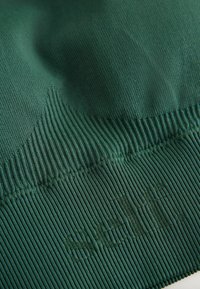 Material verde închis cu textură nervurată, având o marcă subtilă în partea de jos. Suprafață netedă cu elasticitate pentru confort.