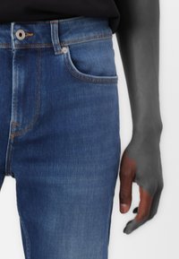 Dark blue denim jeans with a fitted design, featuring orange stitching, a front pocket, and a metal button closure.