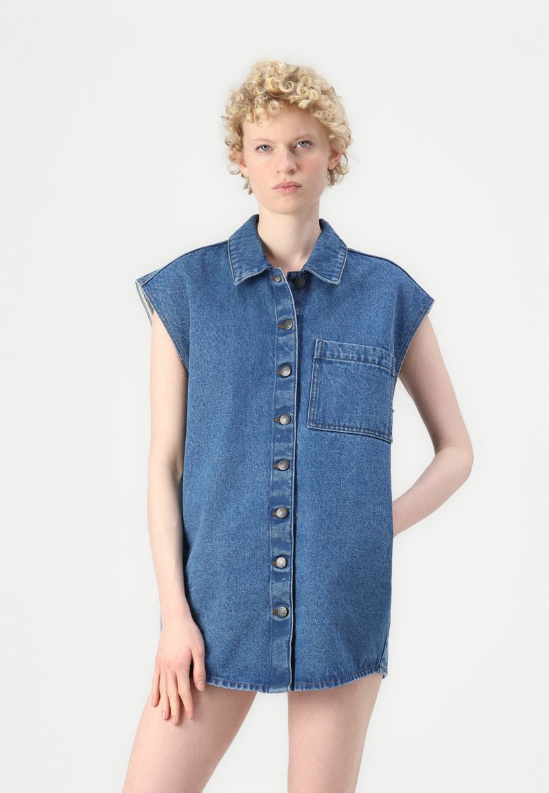 Denim haljina u plavoj boji, s dugmadi sprijeda, džepom na prsima i širokim ramenima s preklopljenim rukavima. Mekani, teksturirani materijal.
