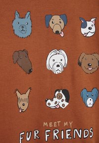 Camicia a maniche corte di colore marrone con nove teste di cani illustrate in vari colori e stili, con la scritta "INCONTRA I MIEI AMICI PELOSI" sotto.