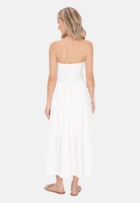 Weißes, trägerloses Maxikleid mit einem gerafften Oberteil und gestuftem Rock. Es ist aus einem leichten, strukturierten Stoff gefertigt und wird mit Riemchensandalen kombiniert.
